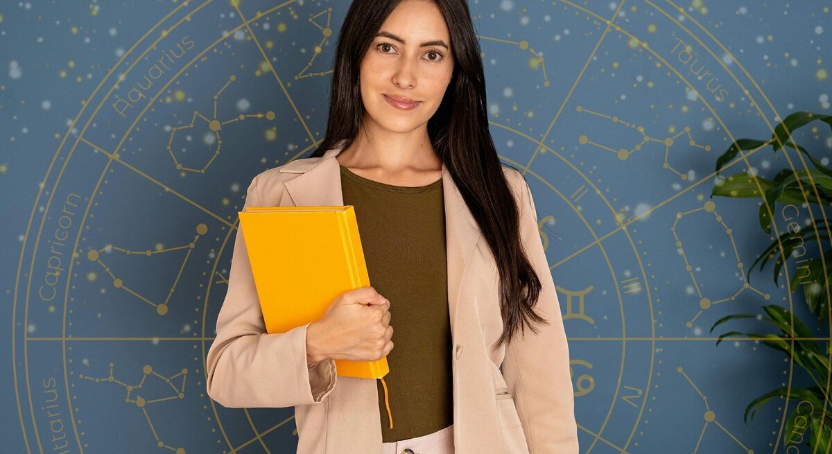 Eine junge Frau mit langen dunklen Haaren und einem freundlichen Lächeln steht vor einem blauen Hintergrund mit goldenen astrologischen Sternzeichen und Konstellationen. Sie trägt einen beigen Blazer über einem olivgrünen Oberteil und hält ein leuchtend gelbes Notizbuch in der Hand. Die Szene vermittelt eine professionelle und zugleich inspirierende Atmosphäre.