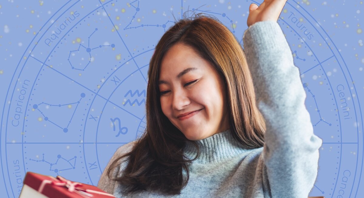 Eine junge Frau mit langem braunem Haar trägt einen hellblauen Strickpullover und hebt freudig eine Hand in die Luft, während sie ein Geschenk mit roter Schleife in der anderen Hand hält. Im Hintergrund ist eine blaue astrologische Sternzeichen-Grafik mit Konstellationen und den Namen der Tierkreiszeichen zu sehen. Die Szene strahlt Glück und Zufriedenheit aus.