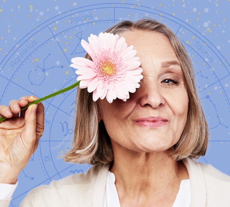 Eine ältere Frau mit schulterlangem, grauem Haar hält eine rosa Blume vor ihr Auge und lächelt sanft. Im Hintergrund ist ein astrologisches Rad mit Sternzeichen und Konstellationen auf einem blauen, sternenübersäten Himmel zu sehen. Das Bild vermittelt eine positive und harmonische Atmosphäre, die Astrologie und Lebensfreude verbindet. | © SHOTPRIME, WinWin.artlab und Mas Water via Canva.com [M]