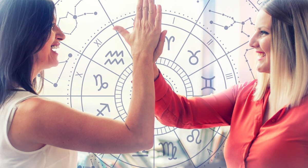  Zwei lächelnde Frauen geben sich ein High-Five vor einem Hintergrund mit einem astrologischen Tierkreis-Muster, das verschiedene Sternzeichen und Symbole zeigt. Die Frau links trägt ein weißes Oberteil, die Frau rechts eine rote Bluse. Die Szene wird von natürlichem Licht durchflutet, das durch Fenster im Hintergrund fällt. Die Geste und die fröhlichen Gesichter vermitteln ein Gefühl von Teamwork und positiver Energie. Der astrologische Hintergrund deutet auf einen Zusammenhang mit Horoskopen oder Sternzeichen hin.