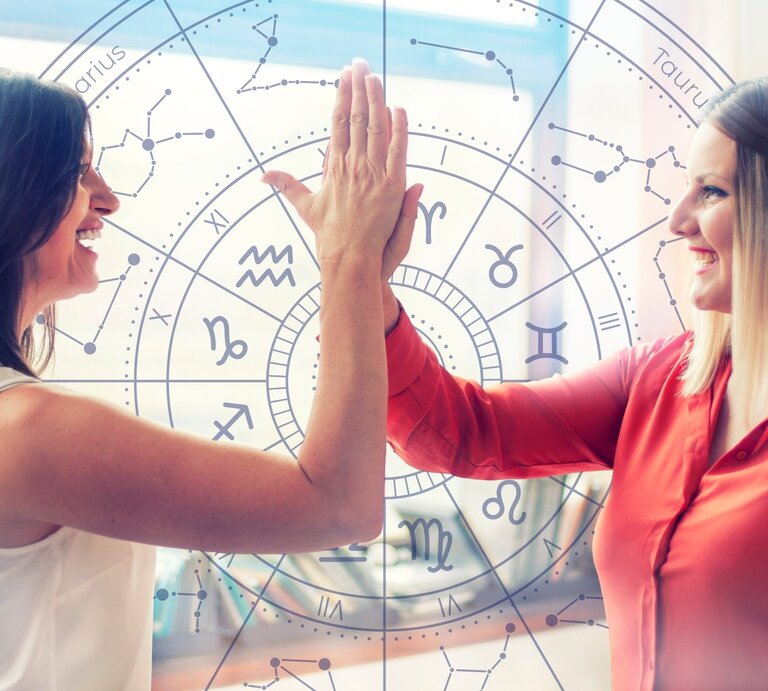  Zwei lächelnde Frauen geben sich ein High-Five vor einem Hintergrund mit einem astrologischen Tierkreis-Muster, das verschiedene Sternzeichen und Symbole zeigt. Die Frau links trägt ein weißes Oberteil, die Frau rechts eine rote Bluse. Die Szene wird von natürlichem Licht durchflutet, das durch Fenster im Hintergrund fällt. Die Geste und die fröhlichen Gesichter vermitteln ein Gefühl von Teamwork und positiver Energie. Der astrologische Hintergrund deutet auf einen Zusammenhang mit Horoskopen oder Sternzeichen hin. | © Getty Images Signature/ draganab und WinWin.artlab via Canva.com [M]
