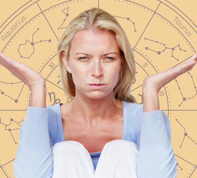 Eine blonde Frau mit ernstem und unzufriedenem Gesichtsausdruck sitzt mit angezogenen Knien und hebt beide Hände fragend oder ratlos nach oben. Sie trägt einen hellblauen Pullover. Im Hintergrund ist ein großes astrologisches Rad mit den Symbolen und Namen der Sternzeichen wie Aquarius, Taurus, Gemini und Capricorn zu sehen. Die warmen, gelblichen Farbtöne des Hintergrunds stehen im Kontrast zu ihrer angespannten Stimmung und vermitteln das Gefühl von Frustration oder Unsicherheit. | © Getty Images/ GlobalStock und WinWIn.artlab via Canva.com [M]