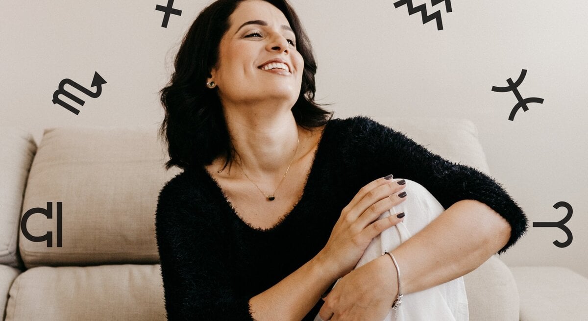Eine Frau sitzt auf einem Sofa und blickt lachend nach oben. Sie sieht glücklich aus und ist umgeben von den astrologischen Symbolen der Tierkreiszeichen.