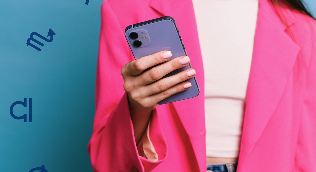 Eine Frau in einem auffälligen pinken Blazer hält ein Smartphone in der Hand. Der Hintergrund ist in einem lebendigen Blau gehalten, und astrologische Symbole schweben dezent um die Szene herum. Die Frau trägt ein schlichtes weißes Top und Jeans, ihre gepflegten Nägel sind in einem natürlichen Ton lackiert. Das Bild vermittelt einen modernen und energiegeladenen Stil mit einem Hauch von Astrologie.