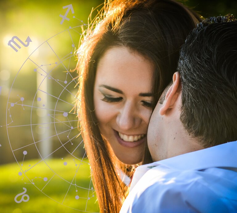 Ein lächelndes Paar in einer innigen Pose im Freien, beleuchtet von warmem Sonnenlicht. Im Hintergrund ist ein astrologisches Rad mit Symbolen der Tierkreiszeichen zu sehen, was auf eine Verbindung zur Astrologie und einem Flirthoroskop hinweist. | © Getty Images/ tdhygino, Gabrielle Scarlett und Chikovnaya via Canva.com [M]