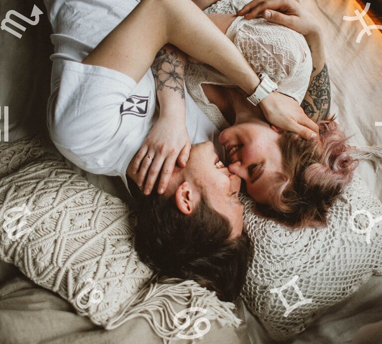 Ein verliebtes Paar liegt eng umschlungen auf einem Bett mit gemütlichen, gehäkelten Kissen. Beide lächeln sich an, während um sie herum astrologische Symbole der Tierkreiszeichen schweben. Die Szene strahlt Intimität, Romantik und eine harmonische Atmosphäre aus. | © The Valeria Ushakova Collection und Chikovnaya via Canva.com [M]