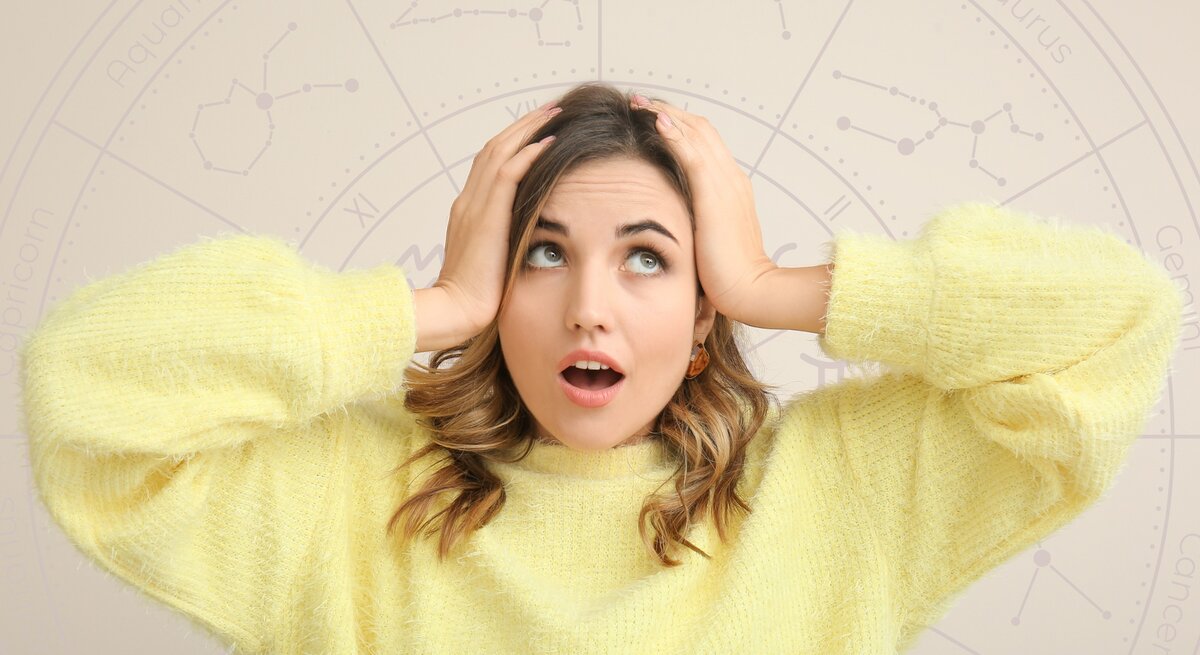 Frau in gelbem Pullover schaut überrascht und hält sich die Hände an den Kopf. Im Hintergrund ist ein astrologisches Rad mit Tierkreiszeichen wie Aquarius, Taurus und Gemini zu sehen.