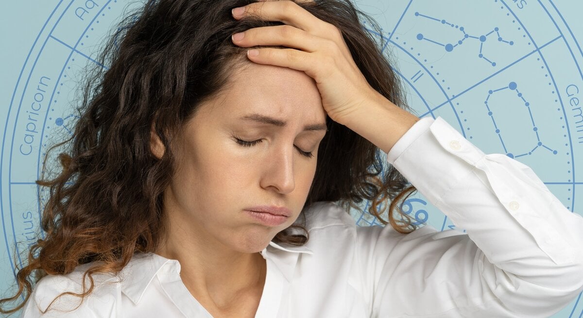 Eine Frau mit lockigem Haar und weißer Bluse hält sich mit geschlossenen Augen die Hand an die Stirn und wirkt erschöpft oder nachdenklich. Im Hintergrund ist ein astrologisches Rad mit den Sternzeichen zu sehen, was auf einen Zusammenhang zwischen ihrem Gemütszustand und astrologischen Einflüssen hinweist.