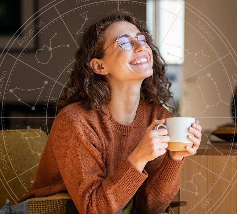 Eine lächelnde Frau mit lockigem Haar und Brille sitzt entspannt auf einem Sofa, hält eine Tasse in den Händen und genießt den Moment. Im Hintergrund ist ein astrologisches Rad mit den Sternzeichen zu sehen, was auf eine positive Verbindung zwischen ihrem Glück und astrologischen Einflüssen hinweist. | © Rido und WinWin.artlab via Canva.com [M]