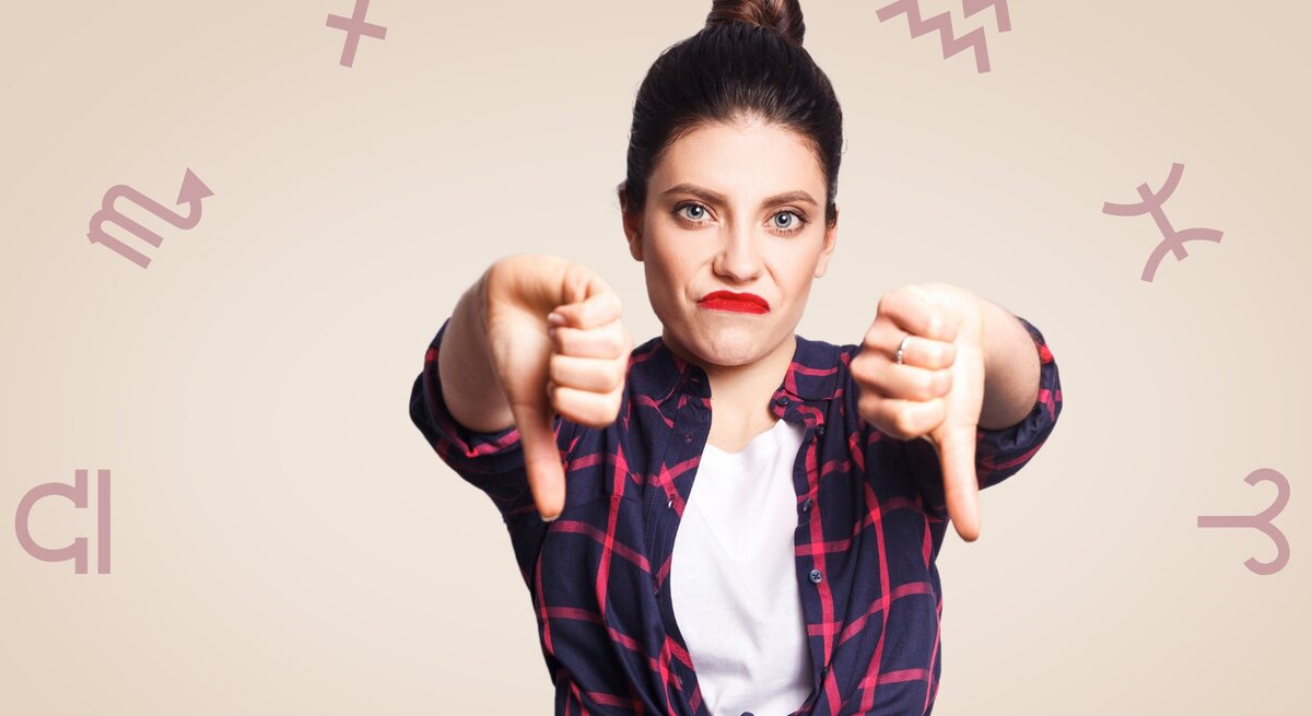 Eine Frau zeigt mit beiden Daumen nach unten und macht ein missmutiges Gesicht. Um sie herum sind astrologische Symbole angeordnet, was eine Verbindung zu einem negativen oder frustrierenden Horoskop-Thema andeutet.