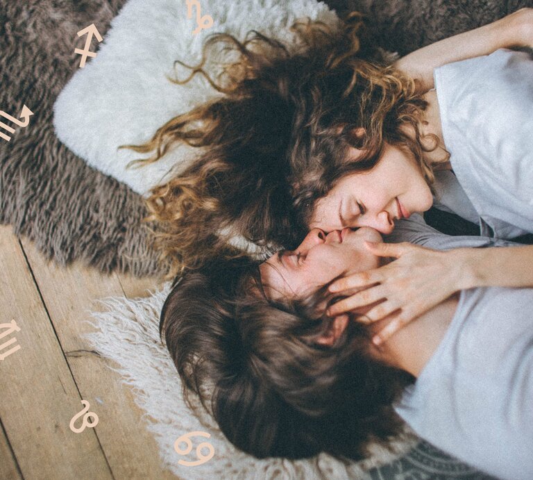 Ein Paar liegt kuschelnd auf einem Teppich, ihre Gesichter sanft aneinander, während sie sich zärtlich berühren. Um sie herum sind astrologische Symbole verstreut, die eine romantische und mystische Stimmung hervorrufen. | © The Valeria Ushakova Collection und Chikovnaya via Canva.com [M]