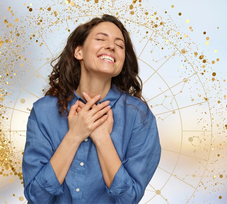 Das Bild zeigt eine junge Frau, die glücklich lächelt und ihre Hände über ihr Herz legt. Sie wirkt dankbar und voller Freude. Im Hintergrund ist ein astrologisches Rad zu sehen, umgeben von goldenen, funkelnden Punkten, die eine festliche und magische Atmosphäre schaffen. Die Frau trägt ein blaues Hemd und die gesamte Szenerie vermittelt ein Gefühl von Zufriedenheit und innerem Glück, das möglicherweise im Zusammenhang mit positiven astrologischen Einflüssen steht. | © dimaberlinphotos, Maryna Stryzhak, Gabrielle Scarlett und Getty Images/ luna4 via Canva.com [M]