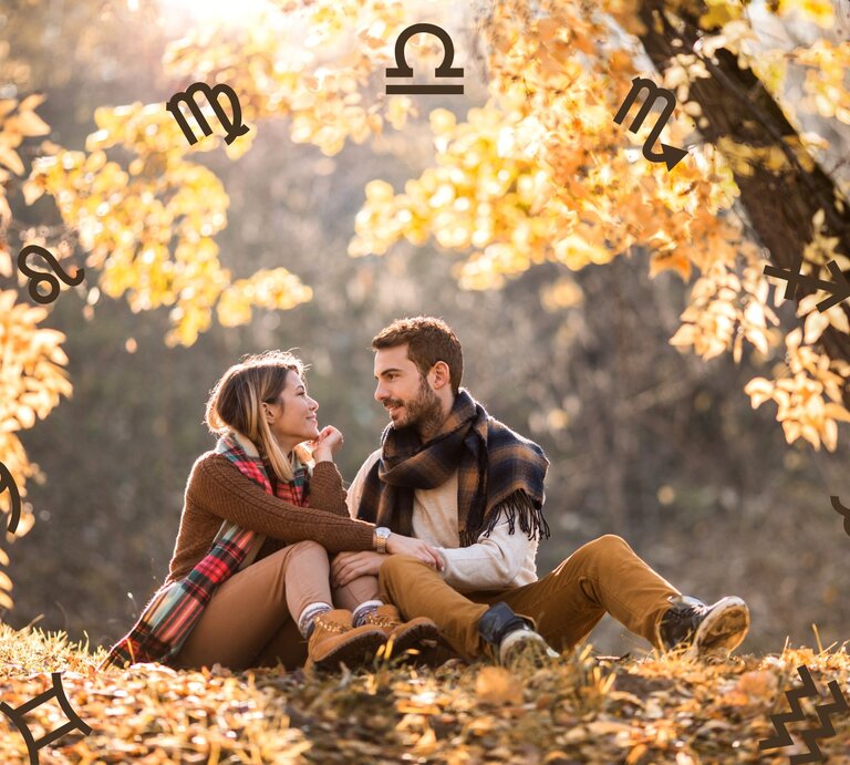  Das Bild zeigt ein Pärchen, das in einer herbstlichen Landschaft unter einem Baum sitzt. Die beiden blicken sich lächelnd an und wirken vertraut und glücklich miteinander. Sie sind warm gekleidet und umgeben von gelb-orangefarbenen Blättern, die die gemütliche Herbstatmosphäre betonen. Rund um die Szene sind Symbole der Sternzeichen wie Widder, Löwe, Waage und andere zu sehen, die das Bild mit einem astrologischen Thema verbinden. | © Getty Images Signature/ skynesher und Chikovnaya via Canva.com [M]