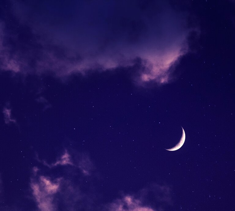Ein Nachthimmel mit einem Sichelmond, der zwischen lila und dunklen Wolken schimmert. Der Himmel ist dunkelblau, mit vereinzelten Sternen, die sichtbar sind. | © Pexels/ Aron Visuals