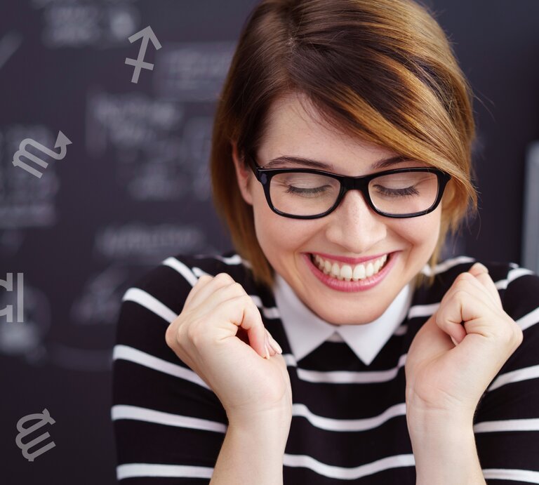 Eine lächelnde Frau mit Brille und gestreiftem Oberteil zeigt eine freudige Reaktion, während sie die Augen geschlossen und die Fäuste leicht geballt hat. Im Hintergrund ist eine Tafel mit verschwommenen, handgeschriebenen Notizen zu sehen. Um sie herum schweben verschiedene Symbole der Tierkreiszeichen, was auf eine astrologische Verbindung oder ein thematisches Setting hinweist. Die Szene vermittelt positive Emotionen, Erfolg oder einen glücklichen Moment. | © Adobe Stock/ contrastwerkstatt und Chikovnaya via Canva.com [M]