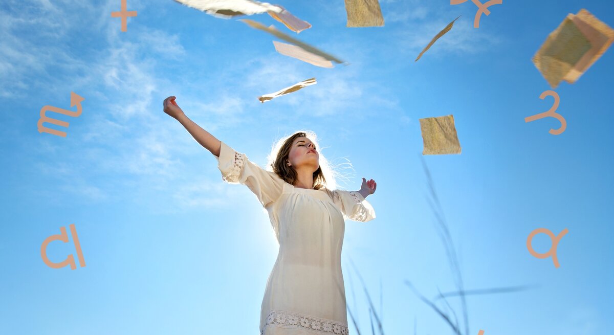 Eine Frau in einem weißen Kleid steht in einer weiten Landschaft unter einem klaren blauen Himmel. Sie hebt ihre Arme in die Luft, während um sie herum Papierblätter und Symbole der Sternzeichen schweben. Die Szene vermittelt ein Gefühl von Freiheit, Leichtigkeit und spiritueller Verbindung.