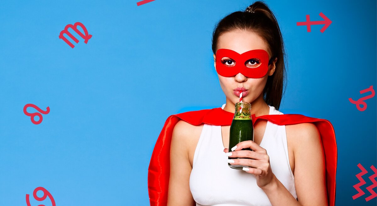 ine junge Frau trägt eine rote Superheldenmaske und ein passendes rotes Cape, während sie einen grünen Smoothie aus einer Flasche mit einem Strohhalm trinkt. Sie trägt ein weißes Sport-Top und steht vor einem blauen Hintergrund, umgeben von roten astrologischen Symbolen verschiedener Sternzeichen.