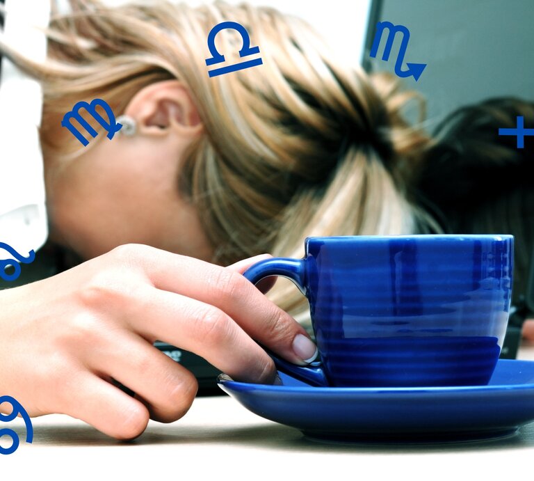 Das Bild zeigt eine erschöpfte Person, deren Kopf auf einem Tisch ruht, während sie eine blaue Tasse in der Hand hält. Im Hintergrund ist ein Laptop zu sehen, was darauf hindeutet, dass die Person möglicherweise überarbeitet ist oder eine Pause einlegt. Um die Person herum schweben verschiedene Sternzeichensymbole, was darauf hindeutet, dass der Artikel wahrscheinlich das Thema Astrologie behandelt und möglicherweise die Auswirkungen der Sternzeichen auf das Wohlbefinden oder die Stressbewältigung im Fokus hat. | ©  Getty Images Signature/ dtokar und Chikovnaya via Canva.com [M]