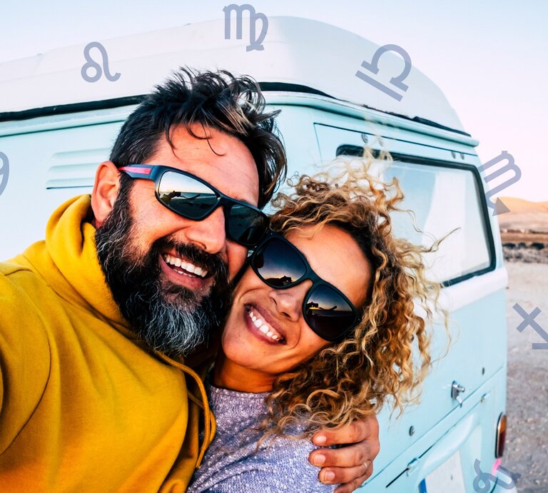 Das Bild zeigt ein glückliches Paar, das Selfie vor einem hellblauen Campervan macht. Beide tragen Sonnenbrillen und lächeln in die Kamera. Der Mann hat dunkles Haar und einen Bart und trägt einen gelben Pullover. Die Frau hat lockiges, blondes Haar und trägt einen grauen Pullover. Im Hintergrund sind eine karge Landschaft und blauer Himmel zu sehen. Um das Paar herum sind verschiedene astrologische Symbole der Tierkreiszeichen auf dem Bild platziert. | © simonapilollatnf und Chikovnaya via Canva.com [M]