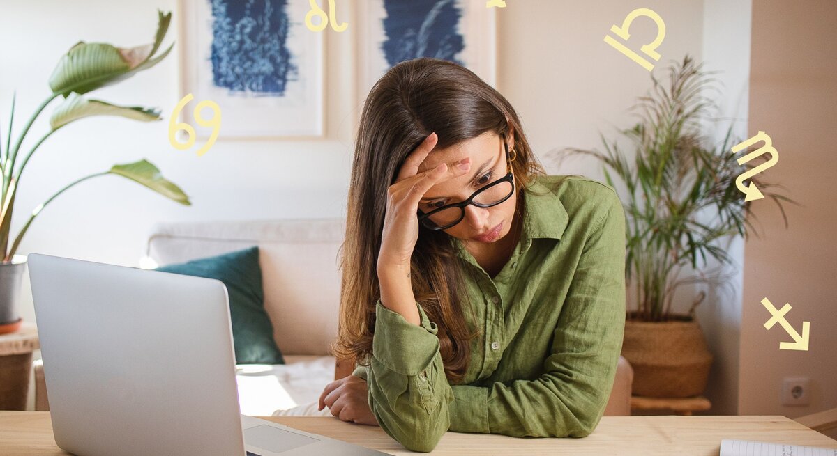 Das Bild zeigt eine Frau, die vor einem Laptop an einem Schreibtisch sitzt und erschöpft oder gestresst wirkt. Sie stützt ihren Kopf mit einer Hand und trägt eine Brille sowie ein grünes Hemd. Auf dem Tisch liegen ein Notizbuch und ein Stift. Im Hintergrund sind Zimmerpflanzen und zwei gerahmte Bilder an der Wand zu sehen. Um sie herum schweben verschiedene astrologische Symbole, was auf einen Zusammenhang mit Astrologie oder Sternzeichen hinweist. Die Szene vermittelt eine Atmosphäre von Müdigkeit oder Überforderung in einer häuslichen oder Arbeitsumgebung.