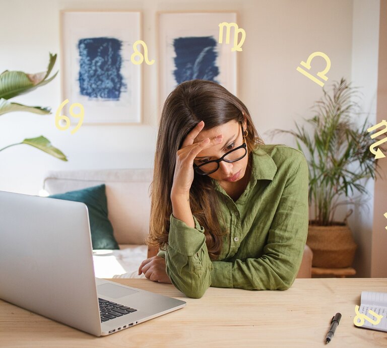 Das Bild zeigt eine Frau, die vor einem Laptop an einem Schreibtisch sitzt und erschöpft oder gestresst wirkt. Sie stützt ihren Kopf mit einer Hand und trägt eine Brille sowie ein grünes Hemd. Auf dem Tisch liegen ein Notizbuch und ein Stift. Im Hintergrund sind Zimmerpflanzen und zwei gerahmte Bilder an der Wand zu sehen. Um sie herum schweben verschiedene astrologische Symbole, was auf einen Zusammenhang mit Astrologie oder Sternzeichen hinweist. Die Szene vermittelt eine Atmosphäre von Müdigkeit oder Überforderung in einer häuslichen oder Arbeitsumgebung. | © Lias Schulz und Chikovnaya via Canva.com [M]