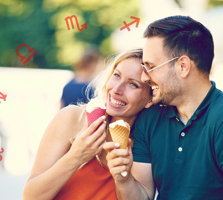 Ein lächelndes Paar genießt Eiscreme im Freien. Die Frau trägt ein orangefarbenes Oberteil und hält ein Eis mit einem rosa Waffelhörnchen, während der Mann ein grünes Poloshirt trägt und ein Eis mit einem braunen Waffelhörnchen hält. Um sie herum sind verschiedene Sternzeichen-Symbole zu sehen, darunter Löwe, Jungfrau, Waage, Skorpion und Schütze. Die Stimmung ist entspannt und fröhlich. | © Getty Images/ grki und Chikovnaya via Canva.com [M]