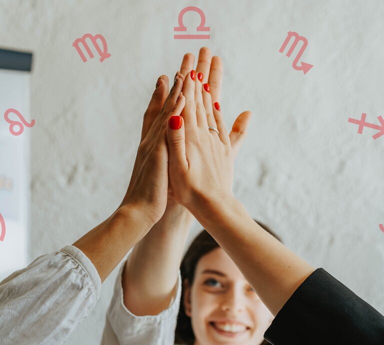 Drei Personen geben sich ein High-Five, wobei nur ihre Arme und Hände sichtbar sind. Eine Person hat rot lackierte Nägel. Im Hintergrund ist eine lächelnde Frau und eine weiße Wand mit astrologischen Symbolen der Tierkreiszeichen Löwe, Jungfrau, Waage, Skorpion, Schütze und Krebs zu sehen. Ein Diagramm ist ebenfalls teilweise sichtbar. | © Pexels/ olia danilevich und Chikovnaya via Camva.com [M] 