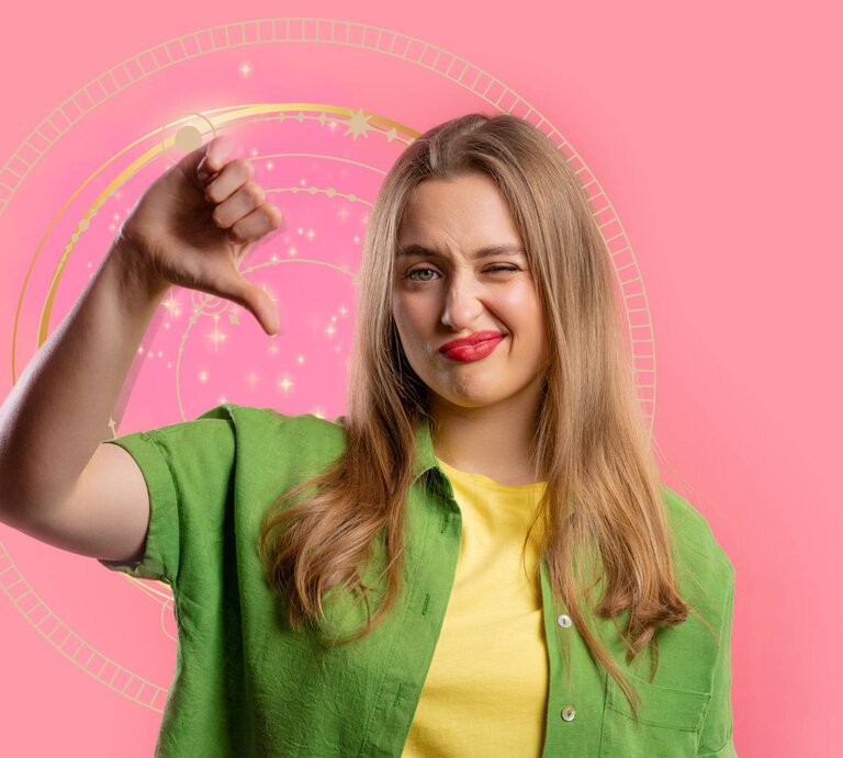 Eine junge Frau mit langen, blonden Haaren steht vor einem rosa Hintergrund mit einem astrologischen Rad. Sie trägt ein grünes Hemd über einem gelben T-Shirt und schaut mit einem unzufriedenen Gesichtsausdruck in die Kamera. Ihre Lippen sind rot geschminkt, und sie zeigt mit ihrem Daumen nach unten, als Zeichen der Missbilligung. | © Kristina Kokhanova/Gettyimages, canvacreativestudio, bombdesign  via Canva.com [M]