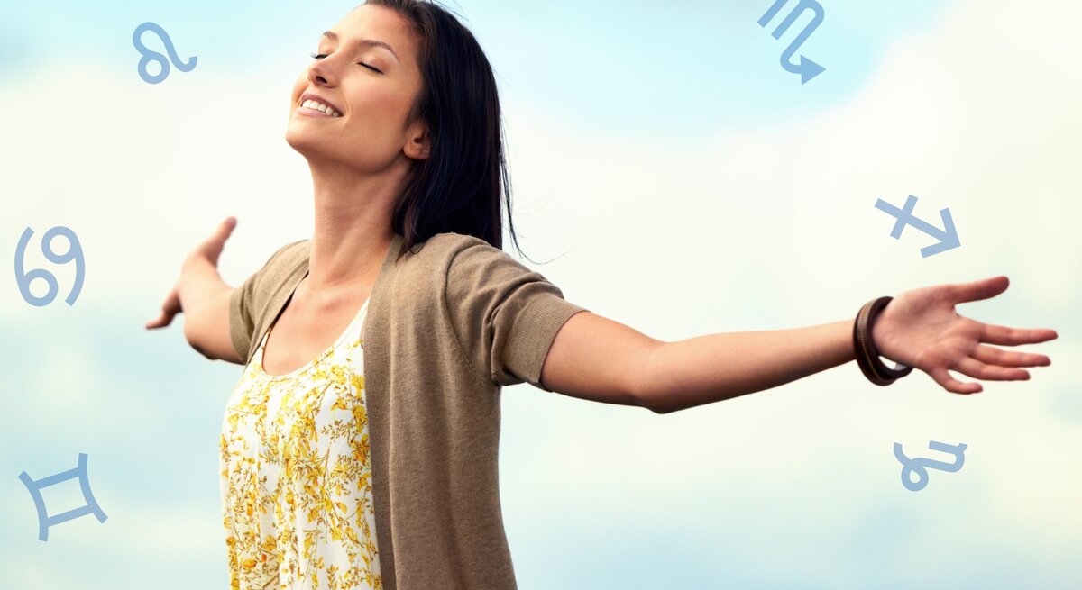 Eine lächelnde Frau steht mit ausgebreiteten Armen im Freien unter einem blauen Himmel. Sie trägt ein weißes Kleid mit gelbem Blumenmuster und eine beige Strickjacke. Um sie herum schweben verschiedene astrologische Symbole, die auf den Tierkreis hinweisen. Die Frau wirkt glücklich und frei.