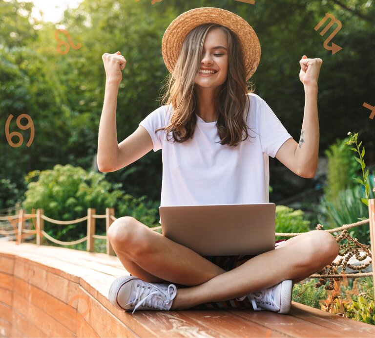 Eine junge Frau sitzt im Schneidersitz draußen in einem Garten mit einem Laptop auf dem Schoß. Sie trägt ein weißes T-Shirt und einen Strohhut und hebt triumphierend die Arme. Um sie herum sind astrologische Symbole von verschiedenen Sternzeichen platziert. | © Dean Drobot und Chikovnaya via Canva.com [M]