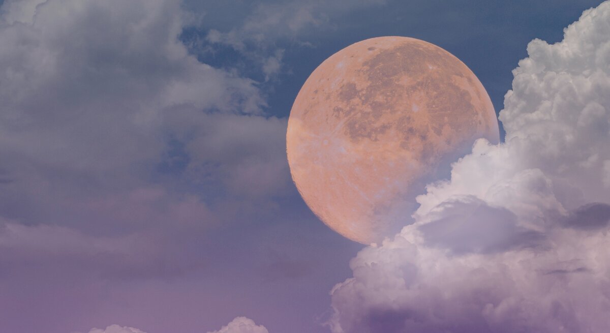 Ein großer, leuchtender Vollmond scheint durch eine teilweise bewölkte Himmelsszene. Der Himmel ist in verschiedenen Blautönen gefärbt, die von einem tiefen, dunklen Blau bis hin zu einem sanften Lila reichen. Die Wolken sind weich und flauschig, in hellen Weiß- und Lilatönen, und umrahmen den Mond, der in warmen, orangefarbenen Tönen leuchtet. Die Szenerie vermittelt eine ruhige und mystische Atmosphäre.