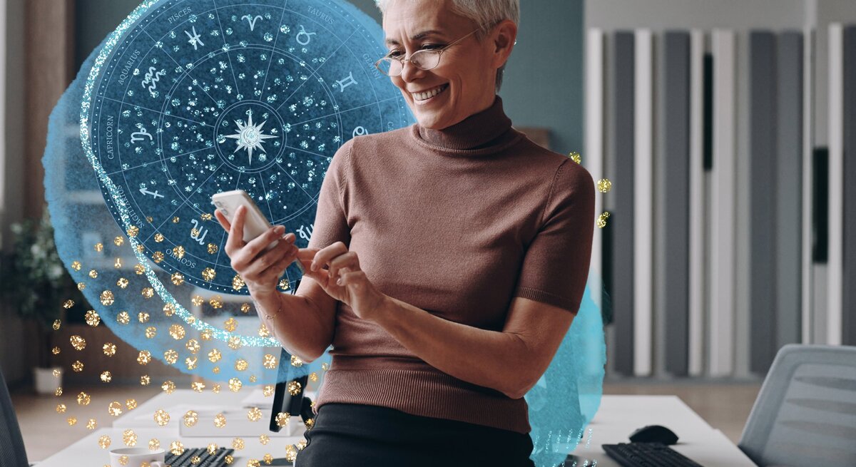 Geschäftsfrau mit grauen Haaren, die ein Smartphone benutzt und lächelt, während sie sich an den Schreibtisch lehnt.