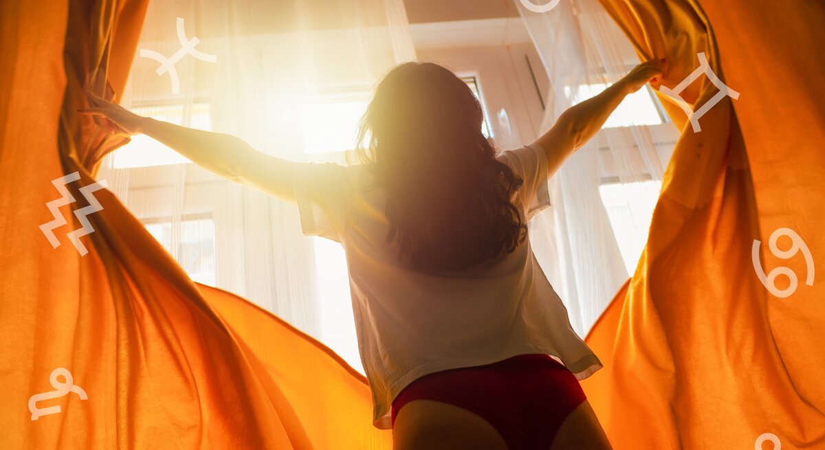 Eine Frau steht mit dem Rücken zur Kamera vor einem sonnendurchfluteten Fenster, die Arme weit geöffnet und zieht die orangefarbenen Vorhänge zurück. Die Morgensonne taucht das Zimmer in ein warmes Licht. Über das Bild sind Astrologie-Symbole verstreut, darunter die Zeichen für Wassermann, Fische, Widder, Stier, Zwillinge und Krebs. Die Szene vermittelt ein Gefühl von Optimismus und neuer Anfang.