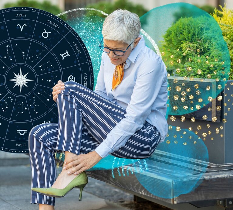 Elegant angezogene Frau, die sich ihren Knöchel hält und Schmerzen zu haben scheint. Sie ist umgeben von blauen astrologischen Symbolen. | © ProfessionalStudioImages/Gettyimages, bombdesign, tartila via Canva.com [M]