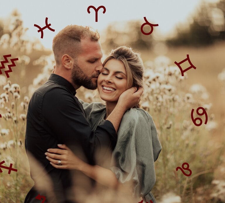 Ein glückliches Paar umarmt sich in einem Feld mit weißen Blüten. Der Mann küsst die Frau sanft an der Schläfe. Um sie herum sind astrologische Symbole wie Wassermann, Widder und andere verteilt. | © Adobe Stock/ Doralin und Chikovnaya via Canva.com [M]