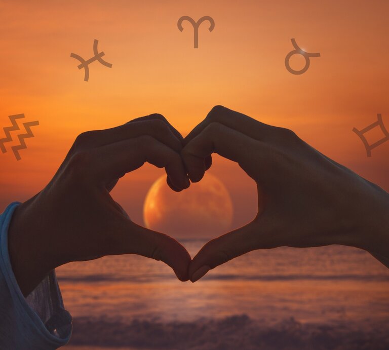 Zwei Hände formen bei Sonnenuntergang ein Herz um eine aufgehende Vollmond-Silhouette am Meer. Im Hintergrund sind astrologische Symbole, einschließlich des Symbols für den Wassermann, Stier, Schütze und Zwillinge, über einen orangefarbenen Himmel verteilt. | © Adobe Stock/ astrosystem und Chikovnaya via Canva.com [M]