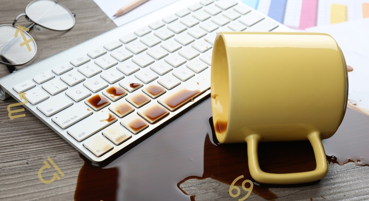 Eine umgestürzte Kaffeetasse liegt auf einem Schreibtisch. Daneben eine Computertastatur und der verschüttete Kaffee darauf.