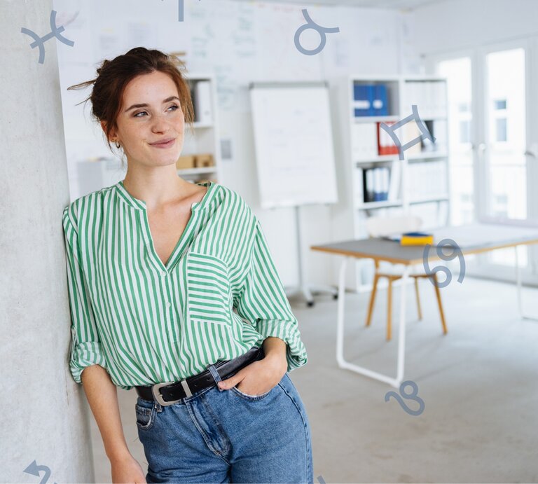 Eine Frau mit weiß-grüner Bluse steht lächelnd an einer Wand. Hinter ihr sieht man ihren Arbeitsplatz. | © Adobe Stock/ contrastwerkstatt und Chikovnaya via Canva.com [M]
