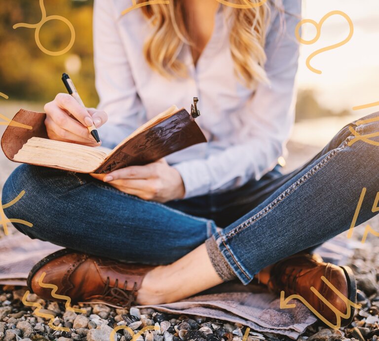 Eine Frau sitzt im Schneidersitz an einem Steinstrand und macht sich Notizen in einem Buch. | © Adobe Stock/ dusanpetkovic1 und Keronyart's Images/ Be keronyart via Canva.com [M]