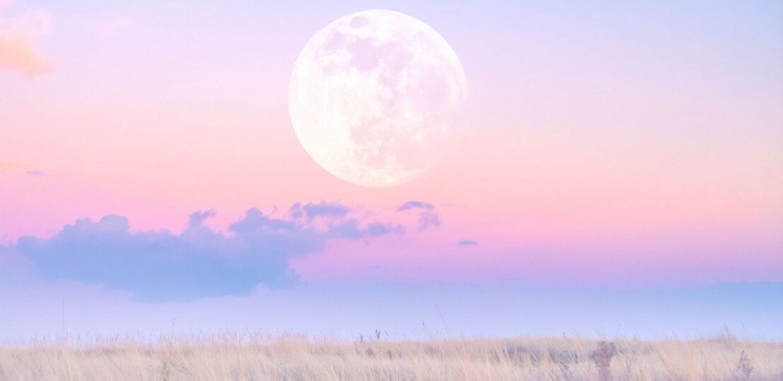 Großer Vollmond über einem pastellrosa‑violetten Himmel mit zarten Wolken; im Vordergrund eine helle, trockene Wiese/Steppe in weichem Abendlicht. | © TrueCreatives via Canva.com