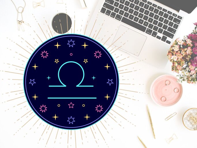 Draufblick auf einen Schreibtisch mit verschiedenen Utensilien wie goldene Kugelschreiber, Sicherheitsnadeln und der Tastatur eines Laptops. Links daneben das grafische Symbol des Sternzeichens Waage in einem dunkelblauen Kreis umgeben von gelben, pinken und hellblauen Sternen. | © Floral Deco, Julia Dreams und warmjuly via Canva.com [M]