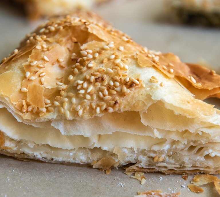Ein Stück Tiropita auf einem Blech mit Backpapier. Alles nah und von vorne fotografiert. | © GettyImages/ AlizadaStudios