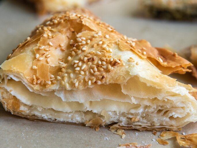 Ein Stück Tiropita auf einem Blech mit Backpapier. Alles nah und von vorne fotografiert. | © GettyImages/ AlizadaStudios