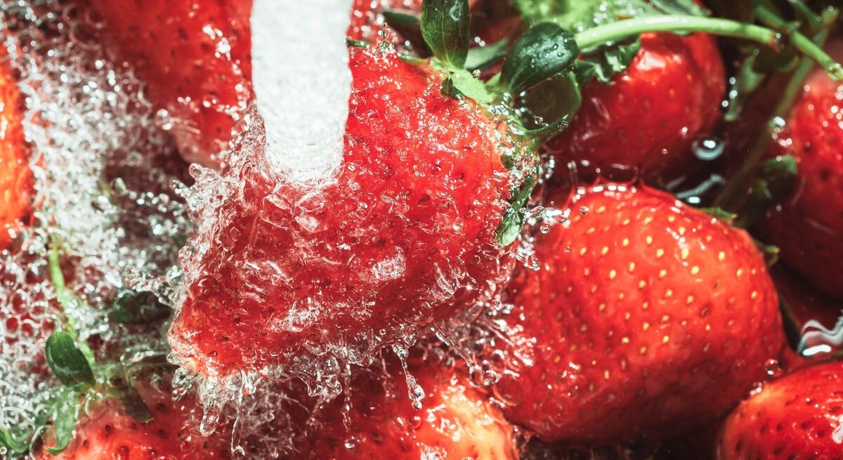 Leuchtend rote Erdbeeren, die energisch unter einem fließenden Wasserstrahl gespült werden.