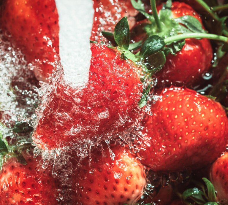 Leuchtend rote Erdbeeren, die energisch unter einem fließenden Wasserstrahl gespült werden. | © Getty Images/MirageC