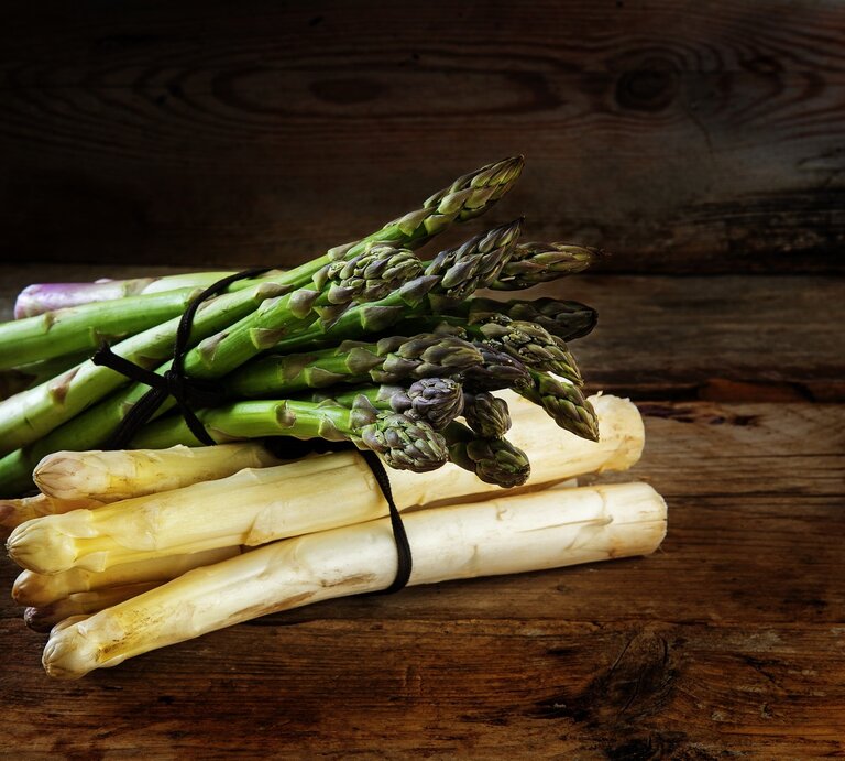 gebundener weißer und grüner Spargel auf Holzuntergrund. | © GettyImages/fermate