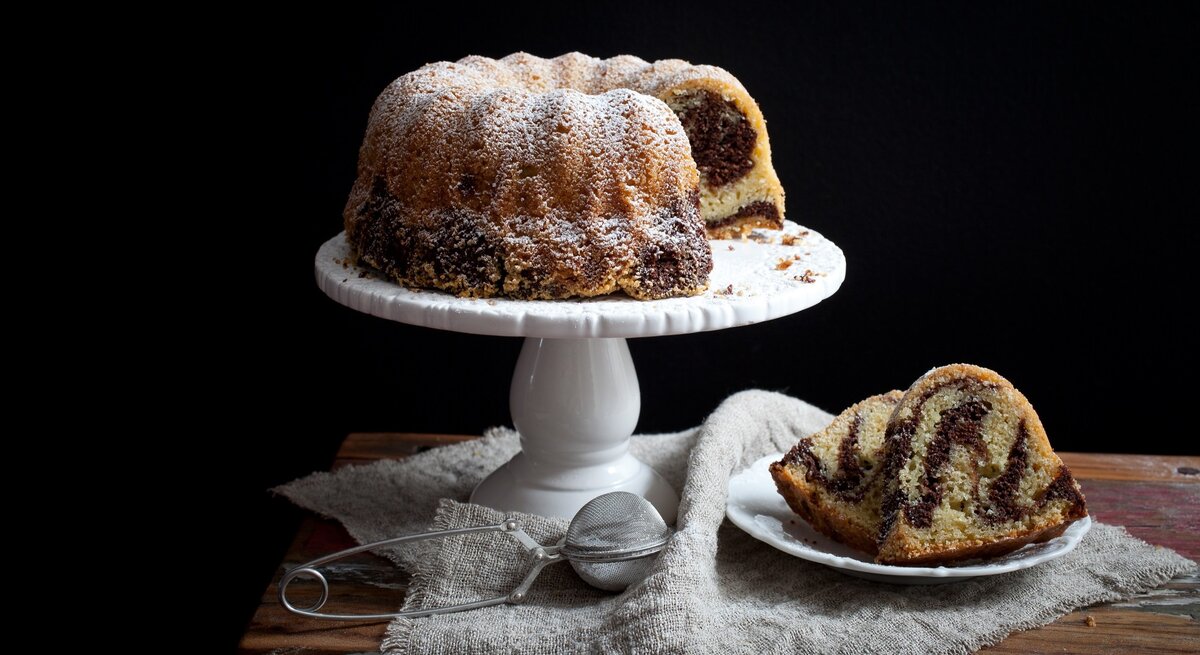 Marmor-Gugelhupf / Tortenständer / runder Teller mit zwei Stück Kuchen / Tuch / Teesieb / Frontalsicht
