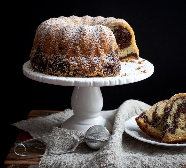 Marmor-Gugelhupf / Tortenständer / runder Teller mit zwei Stück Kuchen / Tuch / Teesieb / Frontalsicht | © Shutterstock / Kati Finell