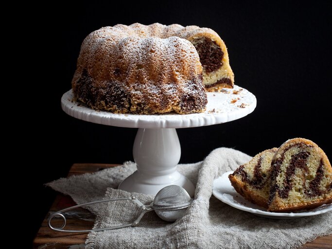 Marmor-Gugelhupf / Tortenständer / runder Teller mit zwei Stück Kuchen / Tuch / Teesieb / Frontalsicht | © Shutterstock / Kati Finell