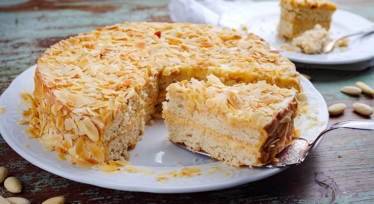 Die Torte auf einem rustikalen Holztisch mit Mandelblättchen drum herum. Alles direkt von vorne fotografiert.